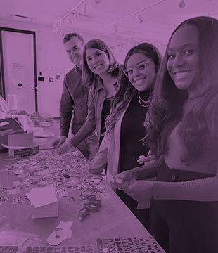Nectarines during our Boston offsite standing, making cards for children cards. Man in back, and three women are lined up next to him. All are smiling at the camera.